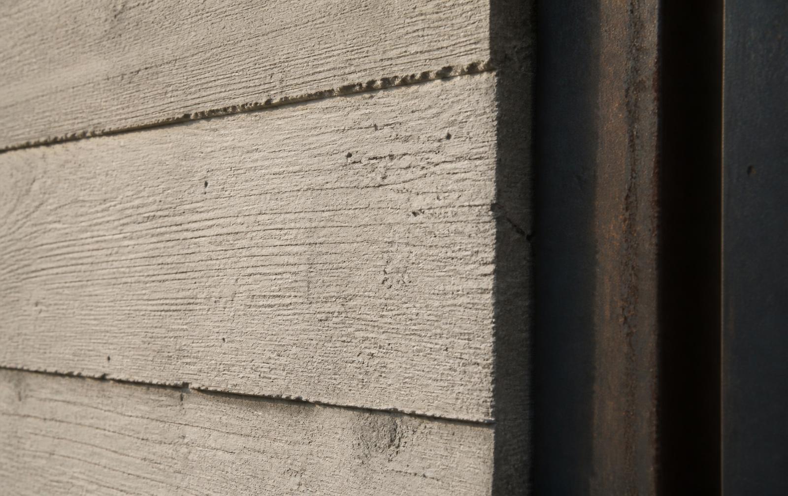 Off-shutter concrete wall meeting a dark steel edge, showing the finished detail of a completed structure